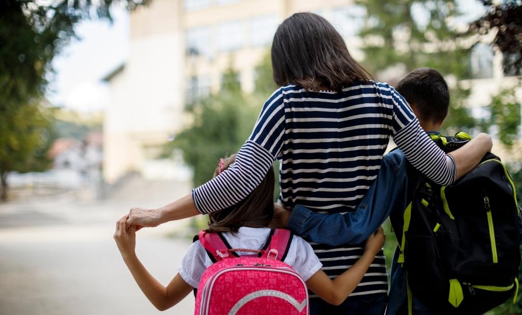 mãe caminhando com duas crianças rumo à escola.