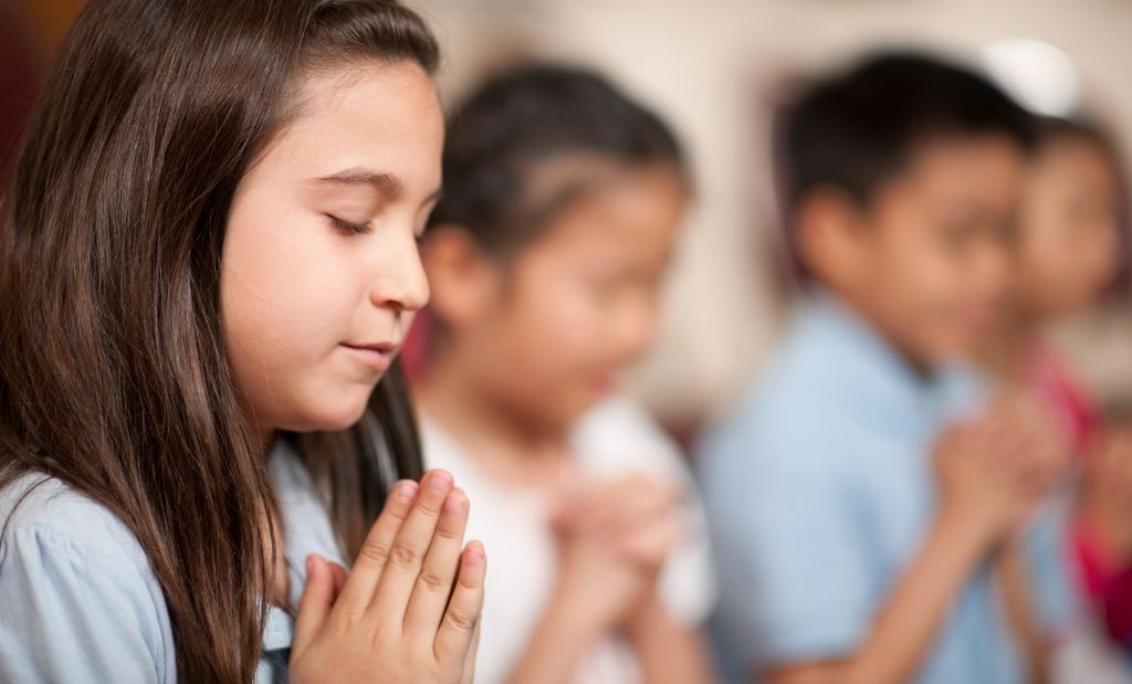 criança com olhos fechados e mãos juntas em posição de oração.