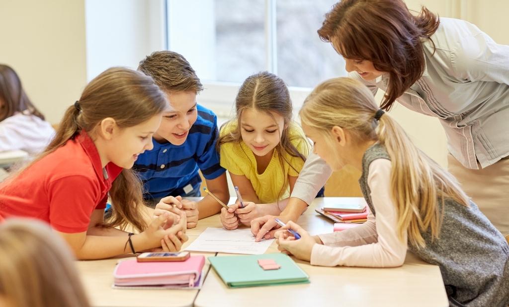 Crianças em sala de aula trabalhando em grupo com apoio da professora.