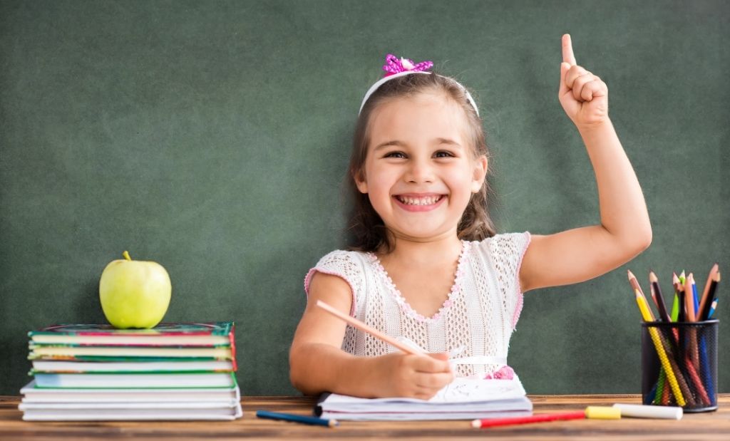 Menina feliz levantando a mão em sala de aula.