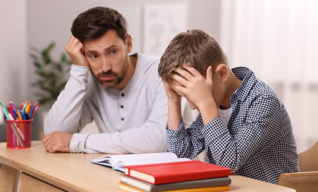 pai preocupado ao lado de criança com dificuldades escolares.