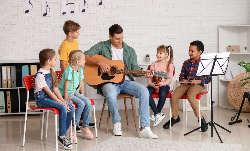Crianças em aula de música com professor tocando violão.