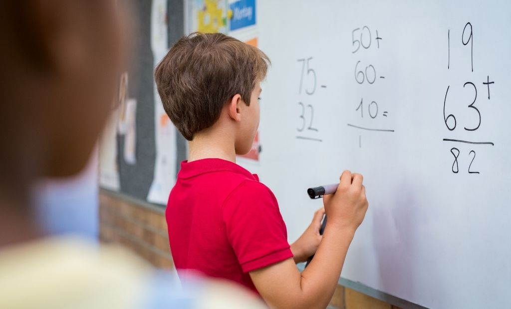 menino resolvendo operações matemáticas no quadro branco.