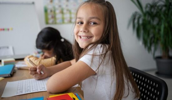 criança sorridente sentada à mesa fazendo atividades de alfabetização