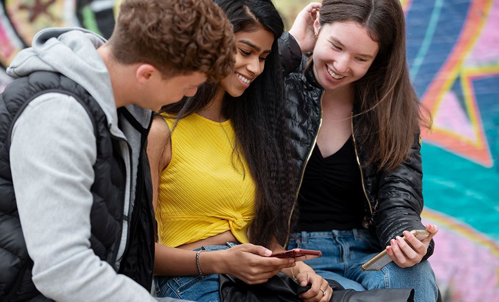 Duas meninas e um menino conversando enquanto olham para a tela de um celular.