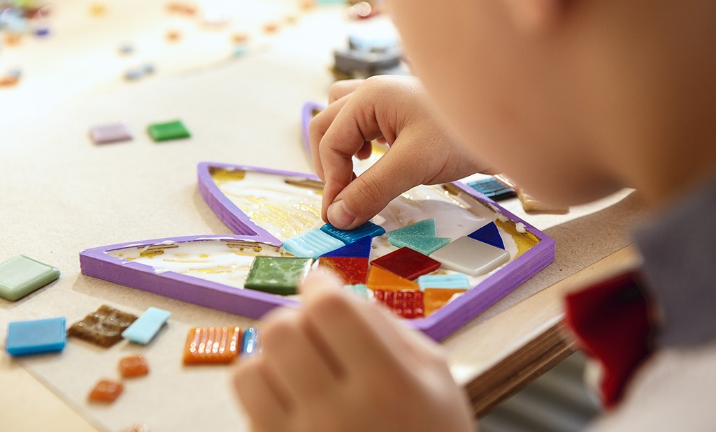 Aluno do ensino fundamental fazendo atividade de colagem com diversas formas geométricas coloridas.