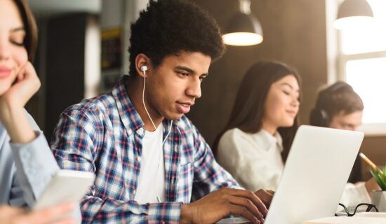 Aluno usando fone de ouvido e computador na biblioteca da escola para estudar com tradutor automático.