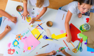 Crianças reunidas em volta de uma mesa, desenhando e colorindo em papéis com canetinhas coloridas.