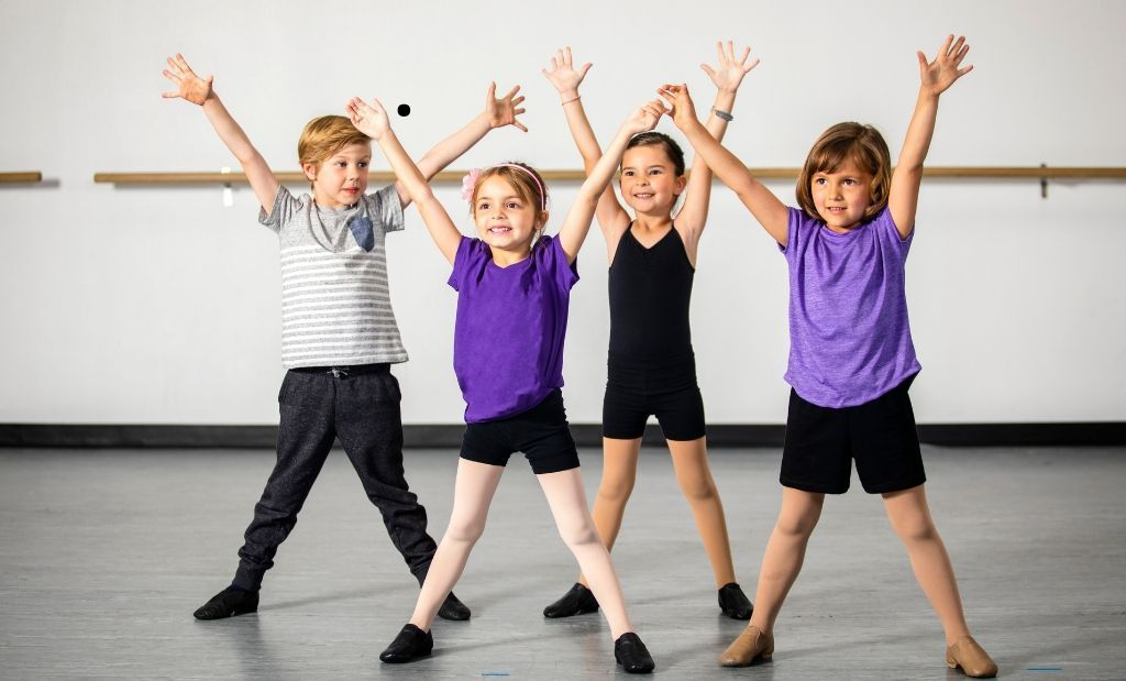 Quatro crianças sorridentes com roupas esportivas participando de uma oficina de dança.