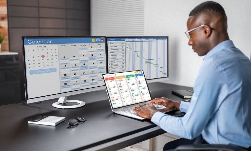 Homem organizando tarefas e calendário em monitores de computador.