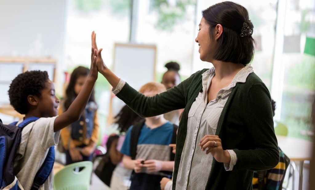 professora cumprimentando um aluno com entusiasmo na sala de aula.