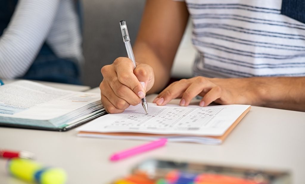 Pessoa escrevendo em um caderno, com foco na mão segurando uma caneta e resolvendo exercícios.