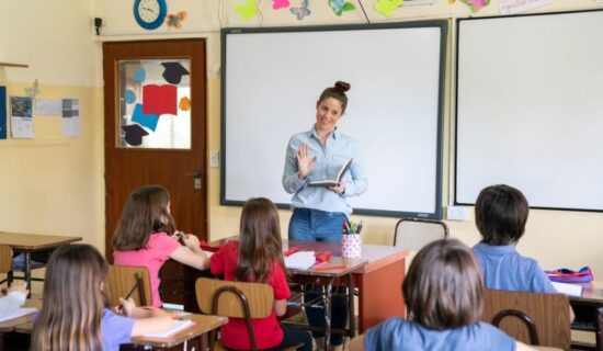 professora ensinando alunos em uma sala de aula presencial.