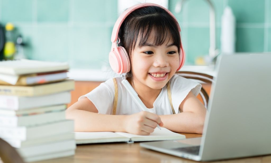 menina usando fones de ouvido enquanto estuda online com um laptop.