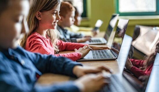 crianças usando laptops em uma sala de aula, aprendendo com tecnologia.