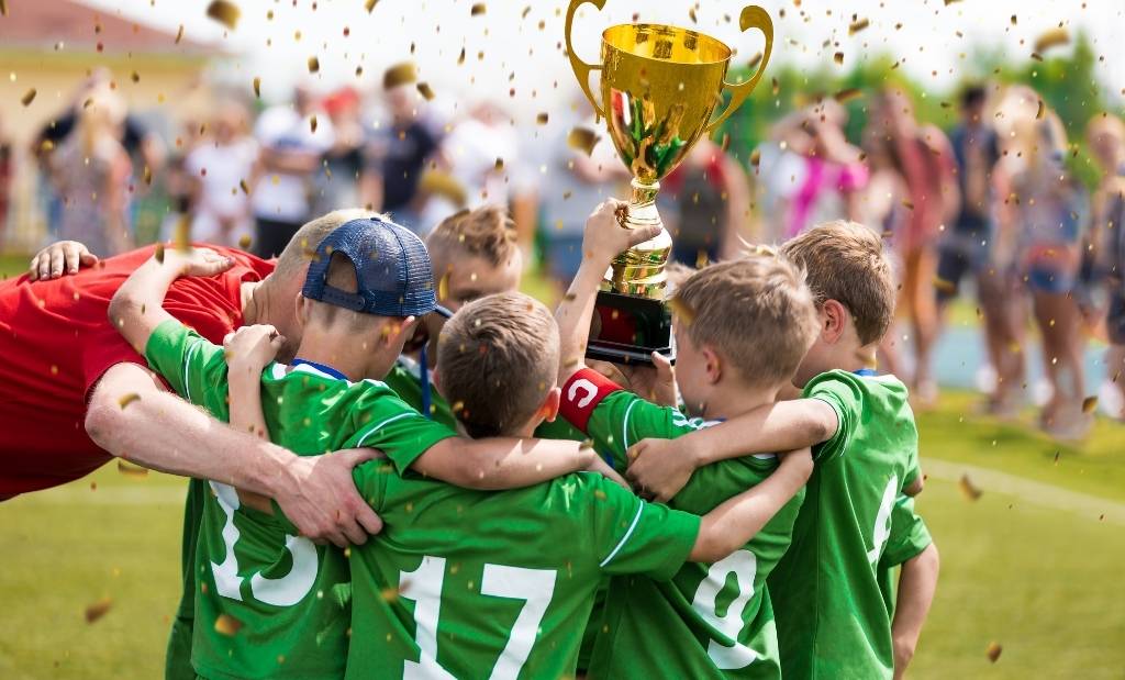equipe infantil de futebol comemorando com troféu após campeonato.