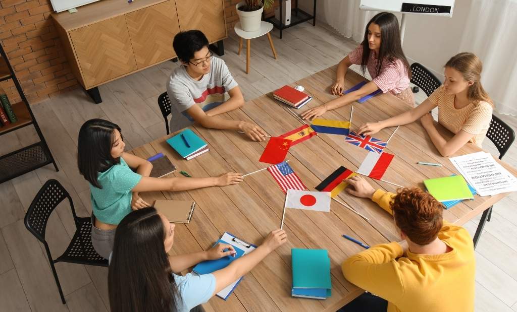grupo de estudantes reunidos em uma sala de aula, segurando pequenas bandeiras de diversos países.